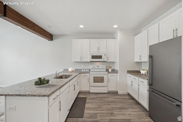 kitchen with white cabinets, a peninsula, a sink, wood finished floors, and white appliances