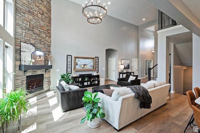 living area featuring arched walkways, a towering ceiling, a stone fireplace, wood-type flooring, and a notable chandelier