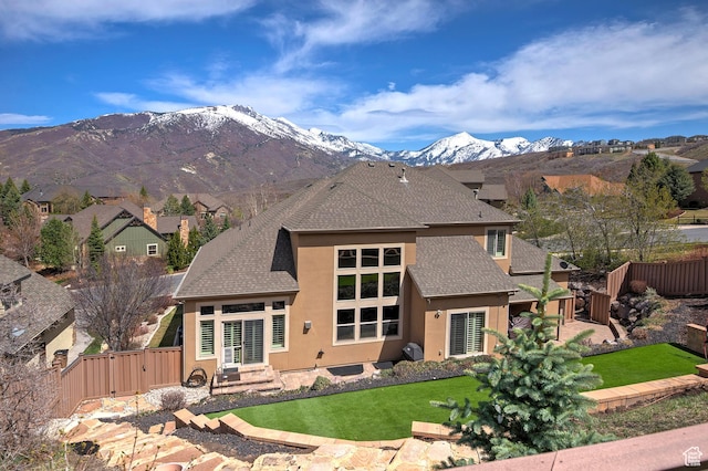 rear view of house featuring a yard, a fenced backyard, roof with shingles, and stucco siding