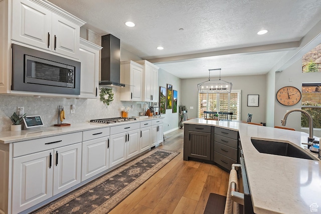kitchen featuring wall chimney exhaust hood, a sink, light countertops, white cabinetry, and stainless steel appliances