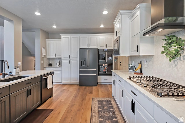 kitchen with a sink, wall chimney range hood, light countertops, and appliances with stainless steel finishes