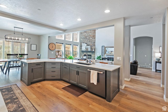 kitchen featuring arched walkways, gray cabinets, dishwasher, a sink, and light countertops
