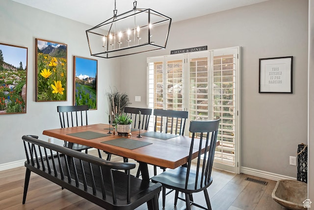 dining area with wood finished floors, an inviting chandelier, baseboards, and visible vents