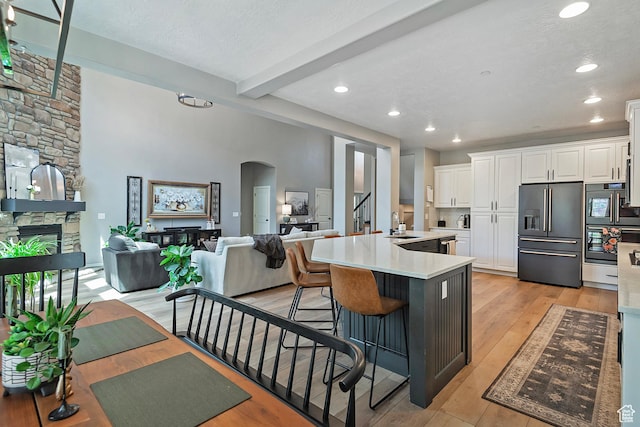 kitchen with a fireplace, arched walkways, high quality fridge, white cabinets, and beam ceiling