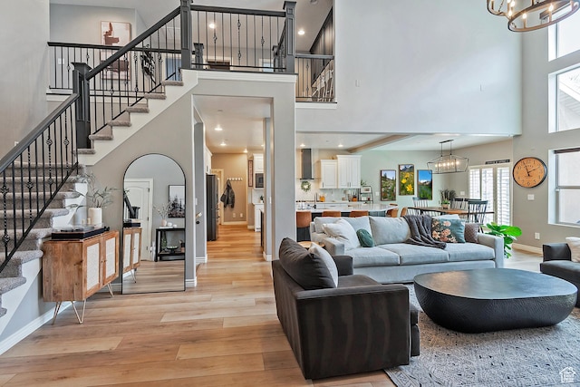 living room featuring light wood-style floors, a chandelier, a high ceiling, stairs, and baseboards
