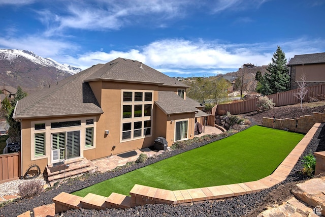 back of house featuring a yard, a fenced backyard, stucco siding, roof with shingles, and a mountain view