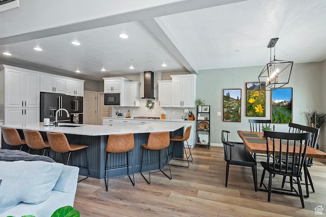 kitchen with tasteful backsplash, wall chimney range hood, white cabinets, black appliances, and a sink