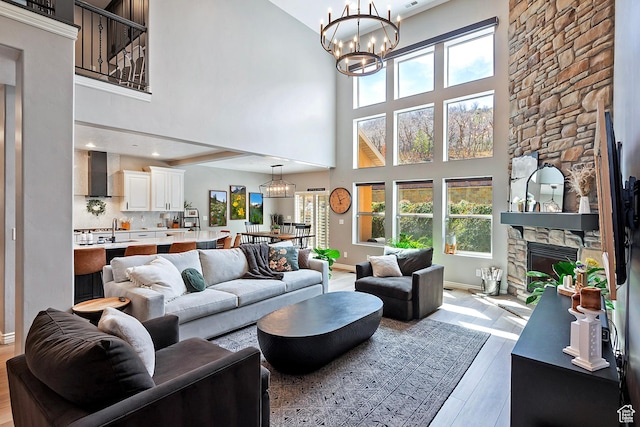 living area featuring a notable chandelier, baseboards, a fireplace, a high ceiling, and wood finished floors