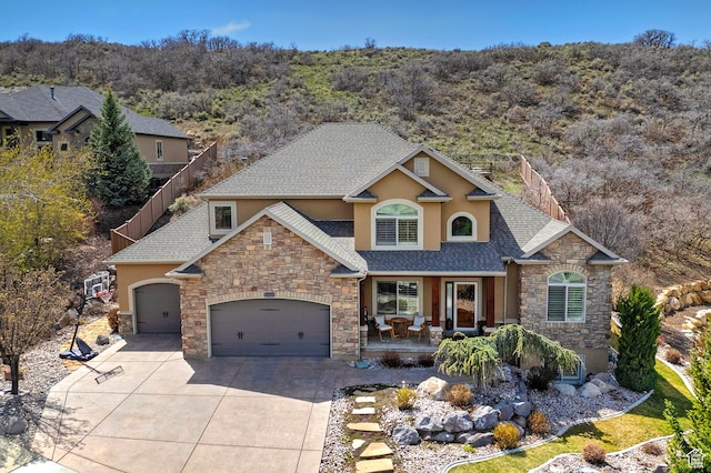 craftsman-style house featuring covered porch, stucco siding, stone siding, an attached garage, and driveway