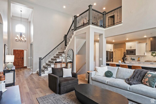 living room with baseboards, a chandelier, stairway, a high ceiling, and light wood finished floors