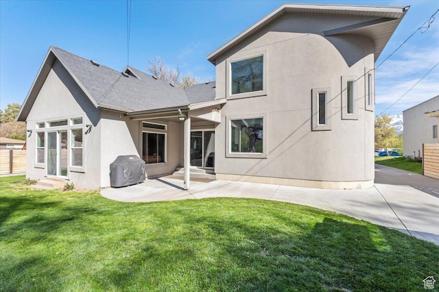 rear view of property featuring entry steps, a lawn, a patio, stucco siding, and roof with shingles