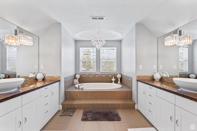 full bath featuring two vanities, a sink, a notable chandelier, and visible vents