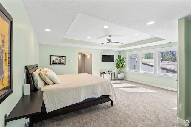 carpeted bedroom with a raised ceiling, arched walkways, baseboards, and recessed lighting