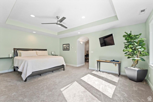 carpeted bedroom with arched walkways, visible vents, baseboards, and a raised ceiling