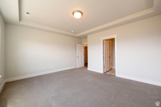 unfurnished bedroom featuring a raised ceiling, light carpet, and baseboards
