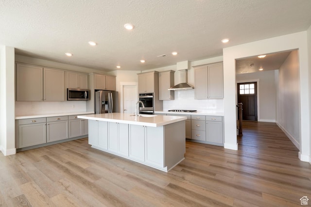 kitchen featuring wall chimney exhaust hood, light wood-type flooring, appliances with stainless steel finishes, decorative backsplash, and gray cabinetry