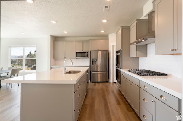 kitchen with gray cabinetry, a sink, wall chimney range hood, and stainless steel appliances