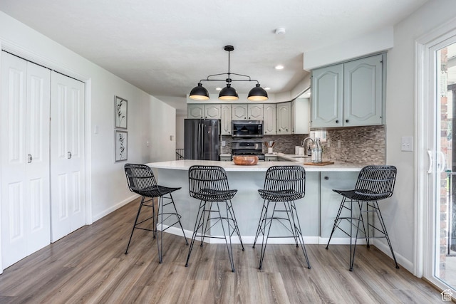 kitchen with a sink, appliances with stainless steel finishes, light wood-style floors, a peninsula, and decorative backsplash