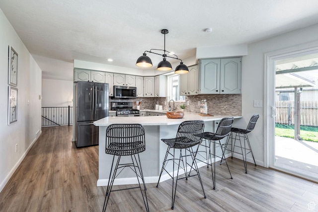 kitchen featuring a peninsula, appliances with stainless steel finishes, wood finished floors, decorative backsplash, and baseboards