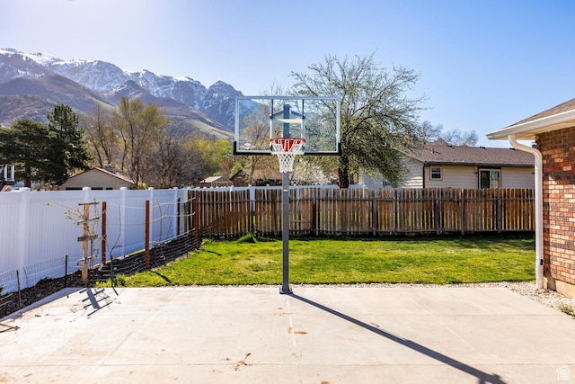 view of sport court with a mountain view, a yard, and a fenced backyard