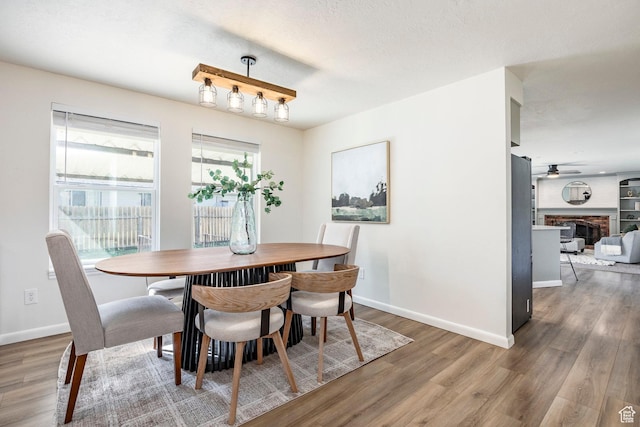 dining space with wood finished floors, ceiling fan, baseboards, and a fireplace
