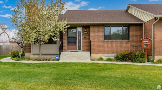 view of front of house with brick siding, a front lawn, and a shingled roof