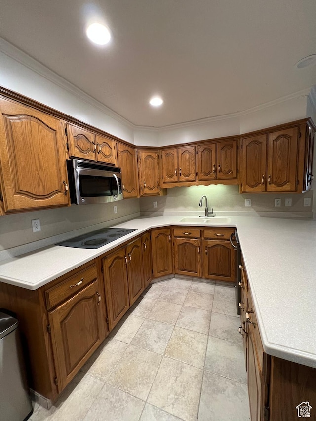 kitchen featuring brown cabinetry, stainless steel microwave, a sink, and black electric cooktop