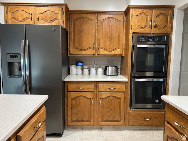 kitchen featuring stainless steel fridge with ice dispenser, light countertops, double oven, and brown cabinets