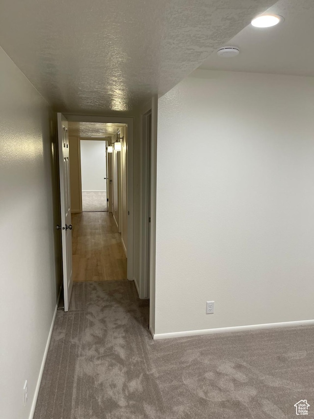 hall with a textured ceiling, carpet flooring, and baseboards