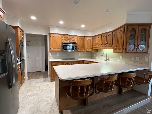 kitchen with a sink, light countertops, appliances with stainless steel finishes, a peninsula, and brown cabinetry