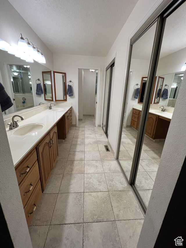full bath featuring double vanity, a textured ceiling, and a sink