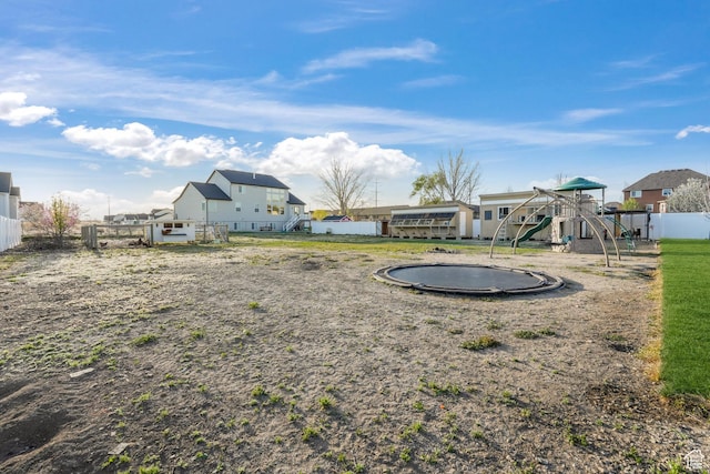 view of yard featuring a trampoline, fence, and a playground