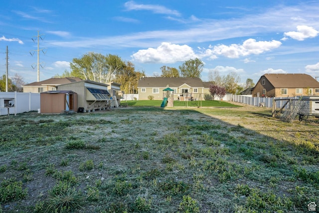 view of yard with a storage shed, a fenced backyard, an outdoor structure, a playground, and a residential view