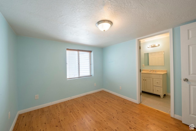 unfurnished bedroom featuring baseboards, a sink, light wood-style floors, a textured ceiling, and connected bathroom