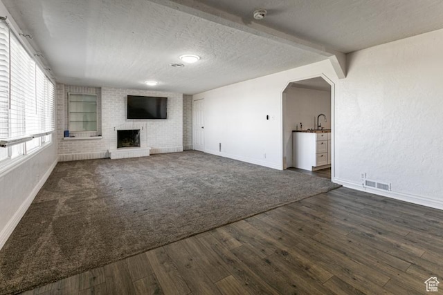 4455 S Aspen Hollow Ln, Holladay, UT 84117 - unfurnished living room with dark wood-style flooring, baseboards, visible vents, a brick fireplace, and a sink
