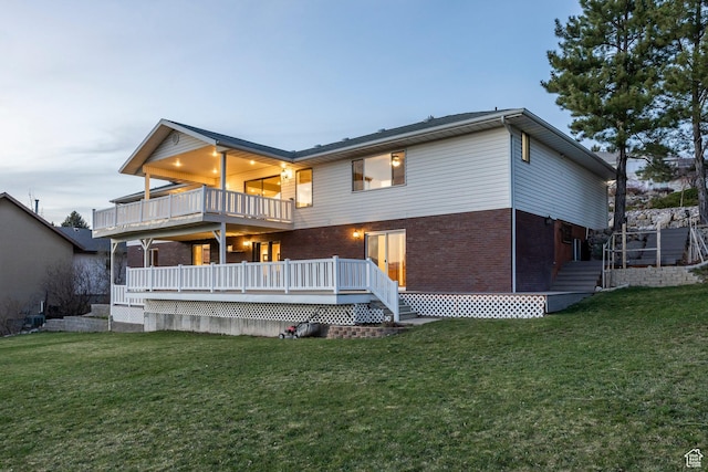 back of property featuring a yard, a deck, brick siding, and a balcony