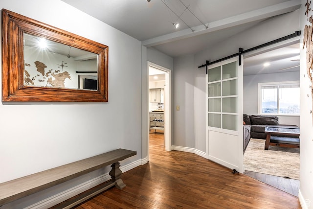 hallway featuring dark wood-type flooring, track lighting, baseboards, and a barn door