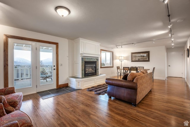 living room featuring baseboards, rail lighting, a fireplace, and dark wood finished floors
