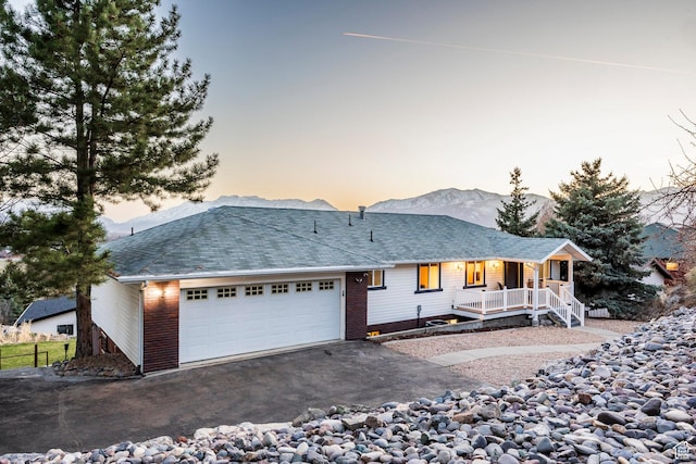 ranch-style house with aphalt driveway, covered porch, roof with shingles, an attached garage, and a mountain view