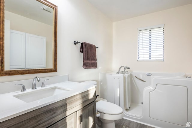 full bath featuring vanity, a bath, toilet, and wood finished floors