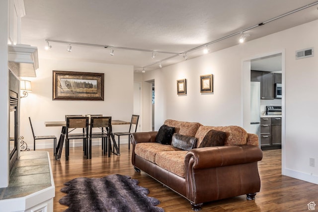 living room with dark wood-style floors, visible vents, baseboards, and track lighting