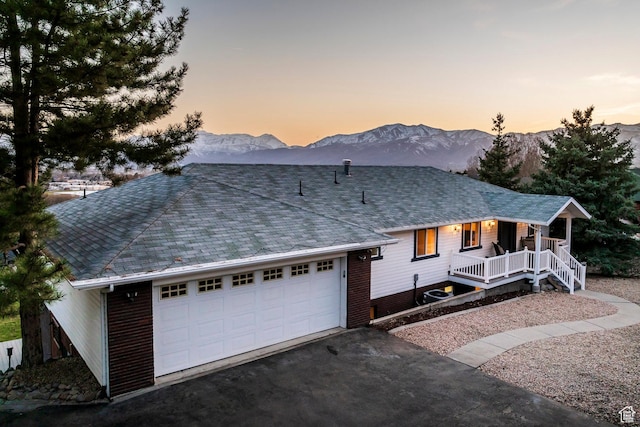 ranch-style house with a mountain view, covered porch, a garage, driveway, and roof with shingles