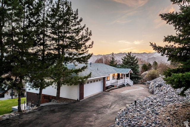 view of side of home featuring aphalt driveway, a mountain view, an attached garage, and covered porch