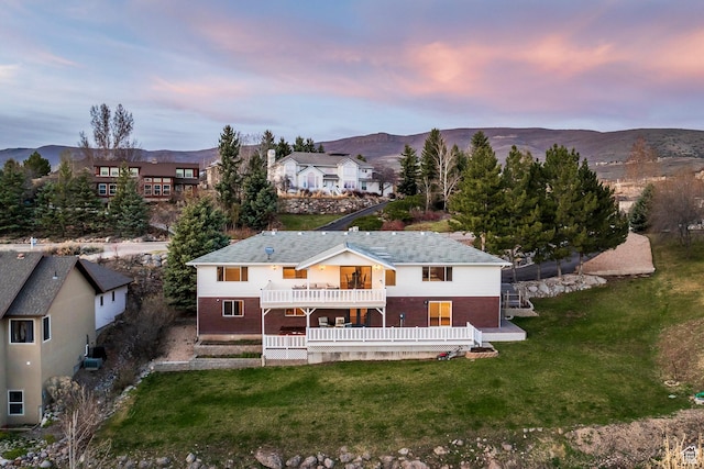 rear view of property with a yard, a deck with mountain view, and a balcony