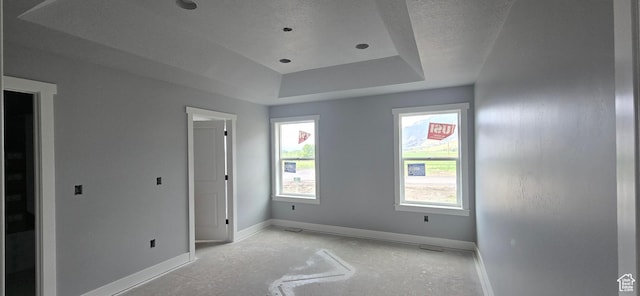 unfurnished bedroom with a tray ceiling, a textured ceiling, and baseboards