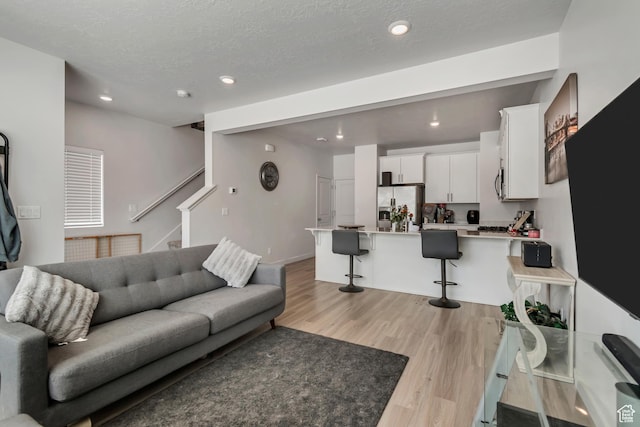living area with recessed lighting, stairway, light wood-style floors, and a textured ceiling