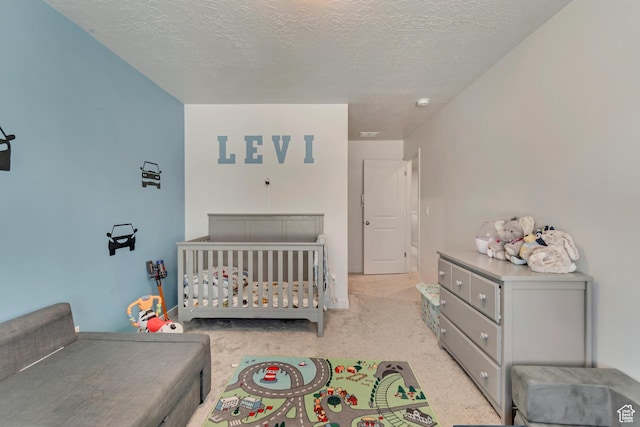 bedroom with a nursery area, light colored carpet, and a textured ceiling