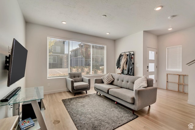 living room with light wood-style flooring, a textured ceiling, baseboards, and recessed lighting