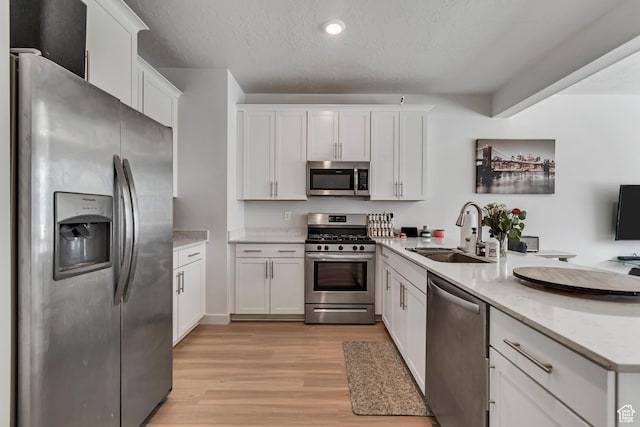 kitchen with a peninsula, white cabinets, light wood-style floors, appliances with stainless steel finishes, and a sink