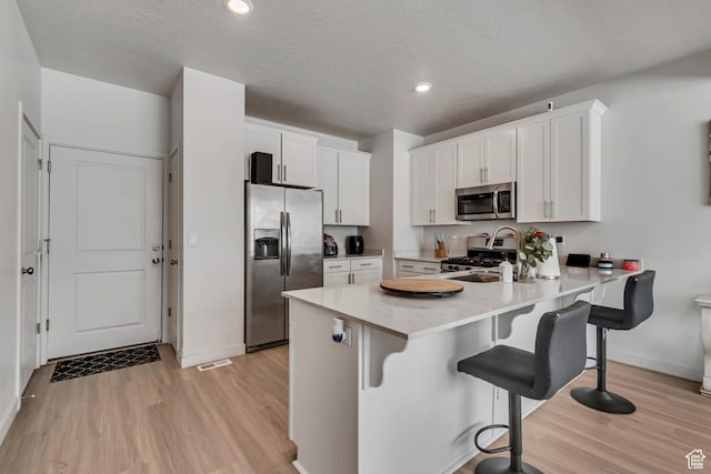 kitchen with baseboards, appliances with stainless steel finishes, a peninsula, white cabinetry, and light wood-style flooring